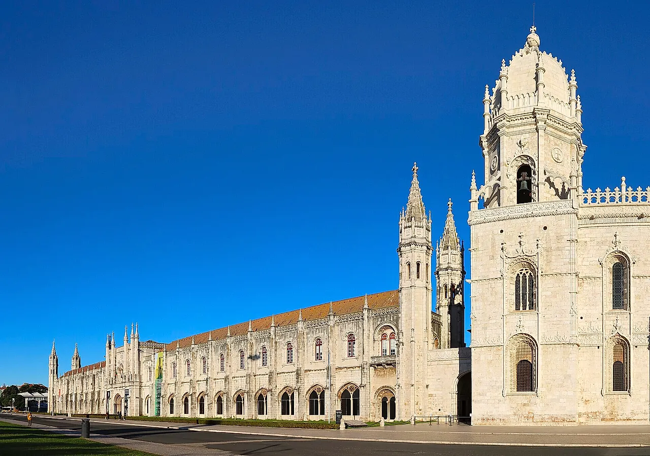 The west wing of the monastery with its slender pinnacled towers and the domed bell tower of the church, in pale stone under a deep blue sky