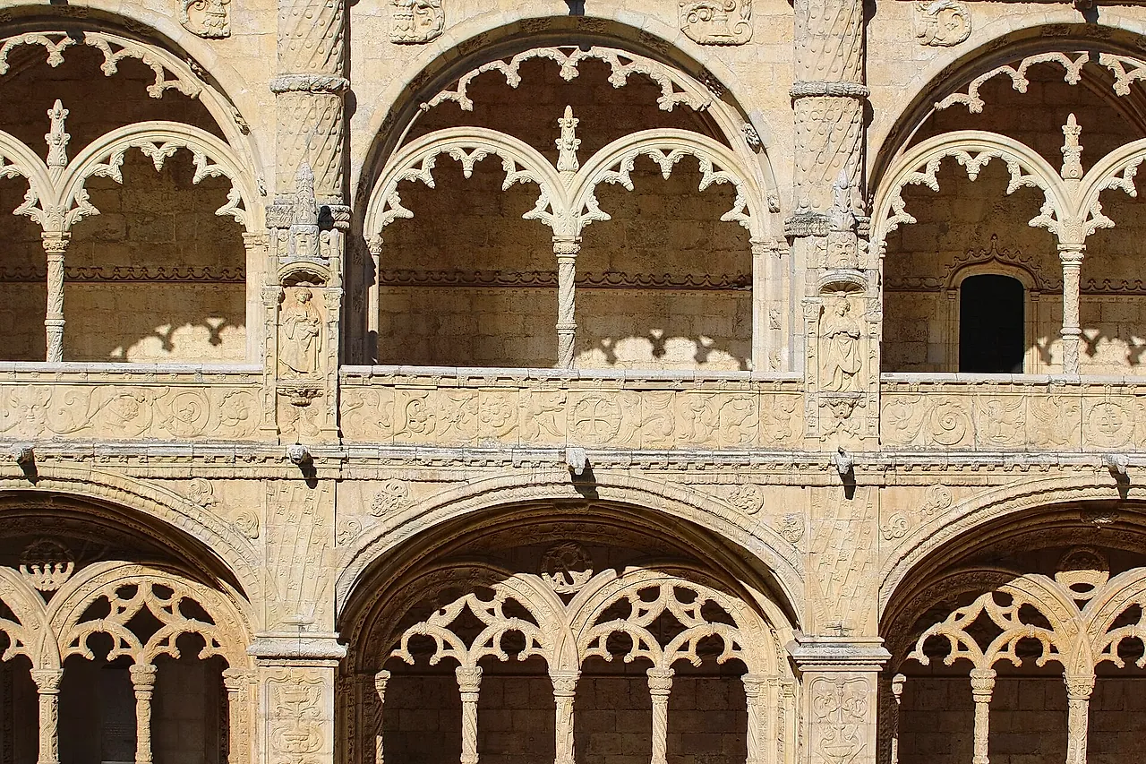 Close view of the two-storey cloister arcades, with lace-like carved arches and slender columns in warm golden stone