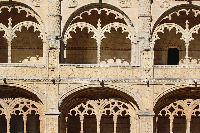 Close view of the two-storey cloister arcades, with lace-like carved arches and slender columns in warm golden stone