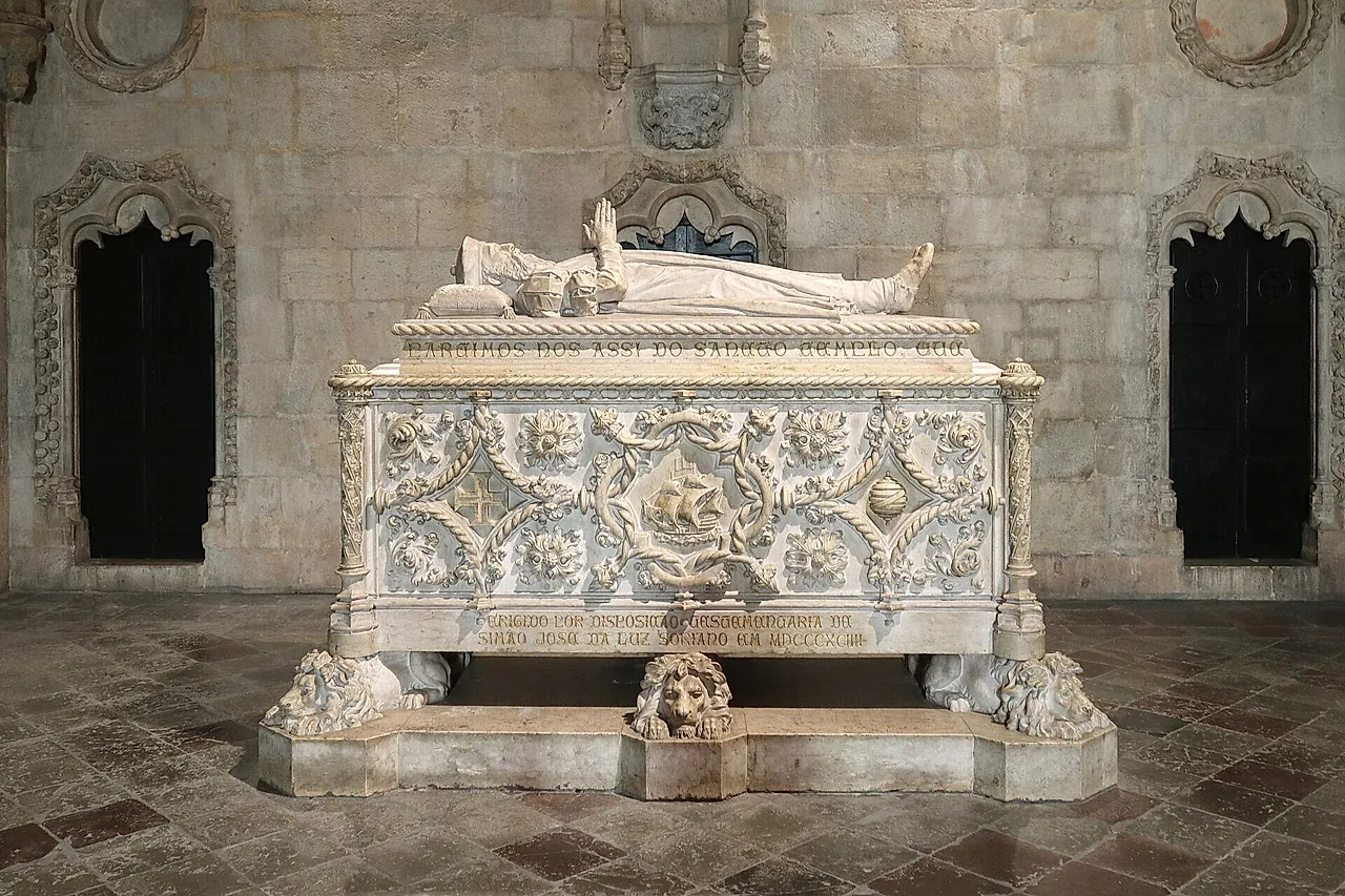 A white marble tomb carved with a ship and leafy ornament, topped by a reclining figure and resting on carved lions, between two dark pointed recesses on a stone floor