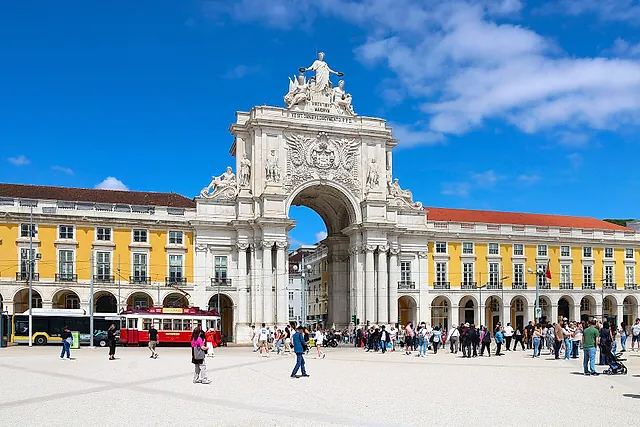 The Rua Augusta Arch with a group of statues on top, framed by the yellow and white arcaded buildings of Praça do Comércio under a blue sky